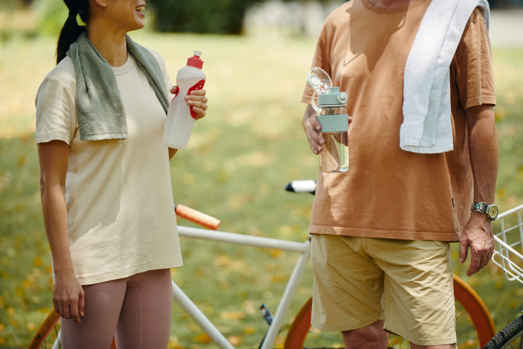 Two people holding water bottles and talking outdoors beside a bicycle