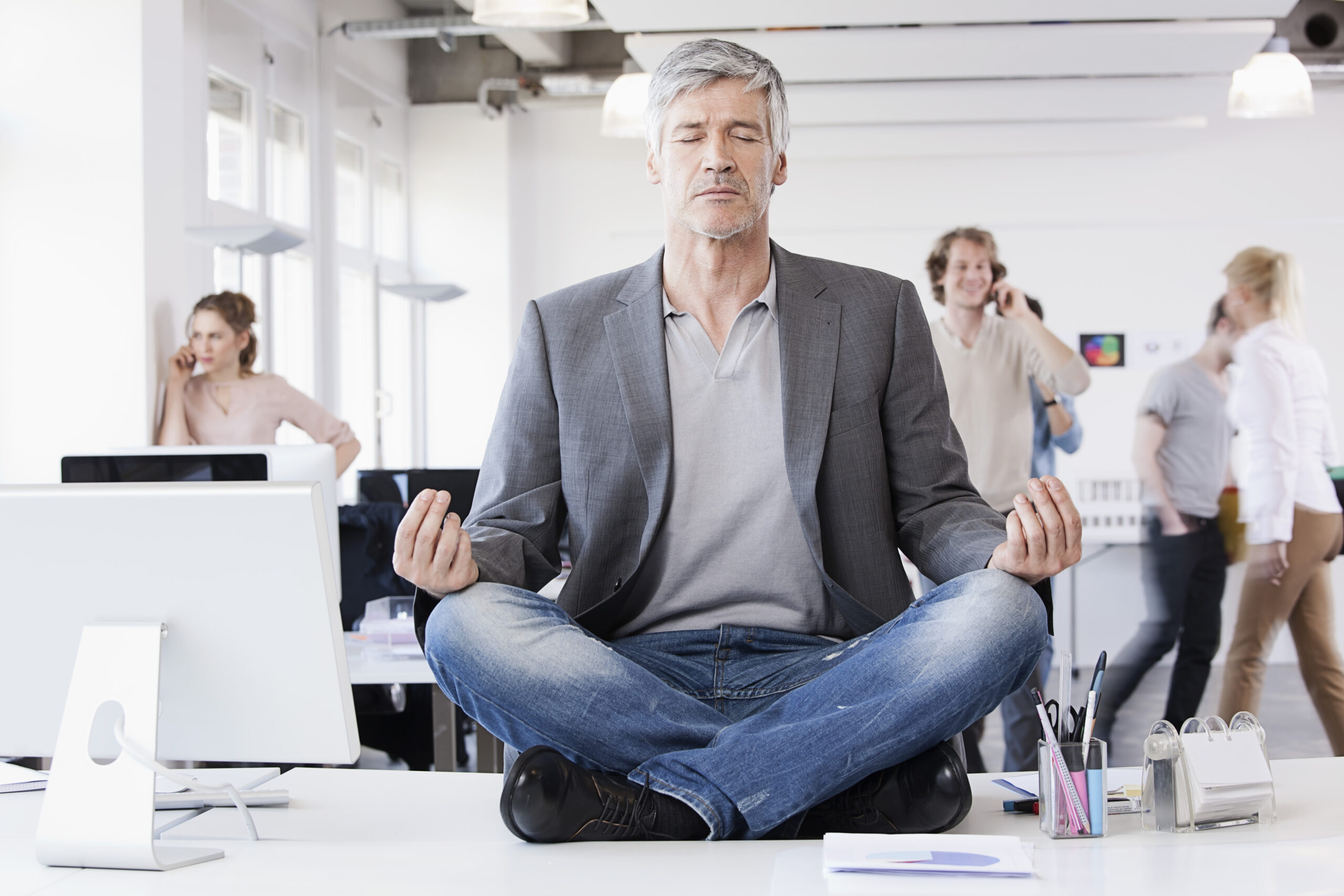 Germany, Bavaria, Munich, Man sitting in lotus position, colleagues in background