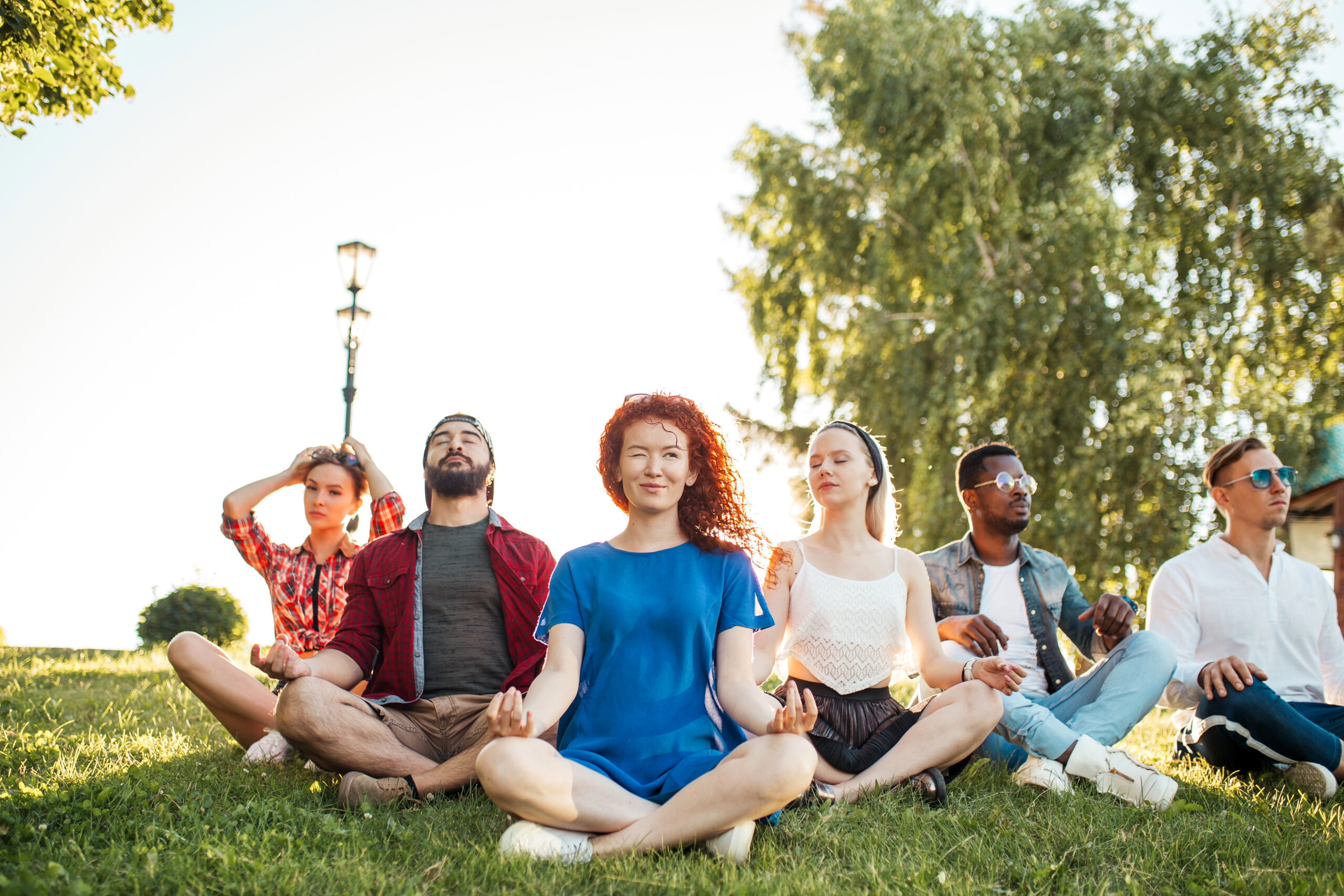 Time for yoga, Attractive young multicultural friends exercising in yoga lotus pose while resting after a long trip in Botanical garden. Multiethnic people dressed in casual summer outdoor clothing.