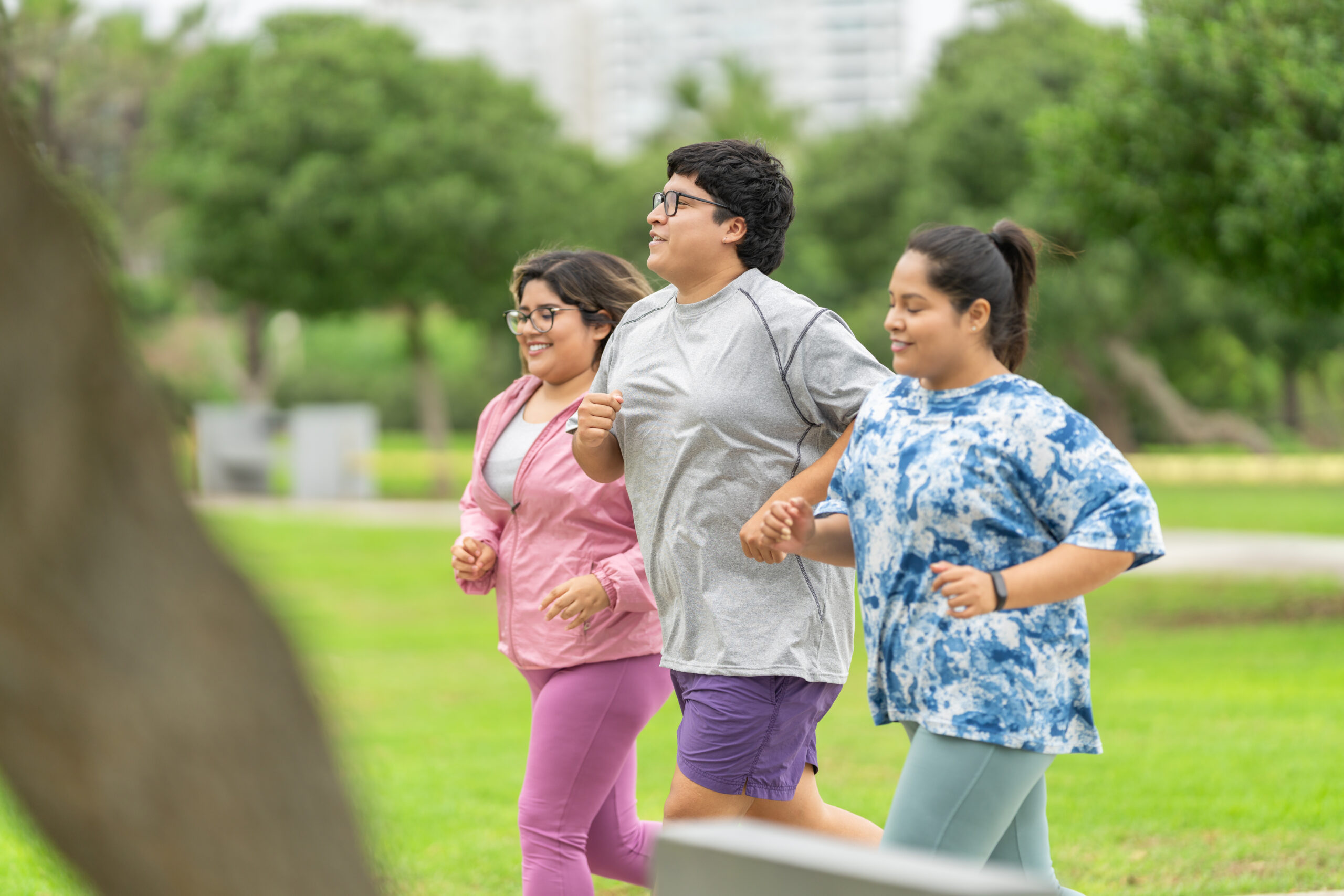 Side view of three overweight friends in sportive clothes running along a park