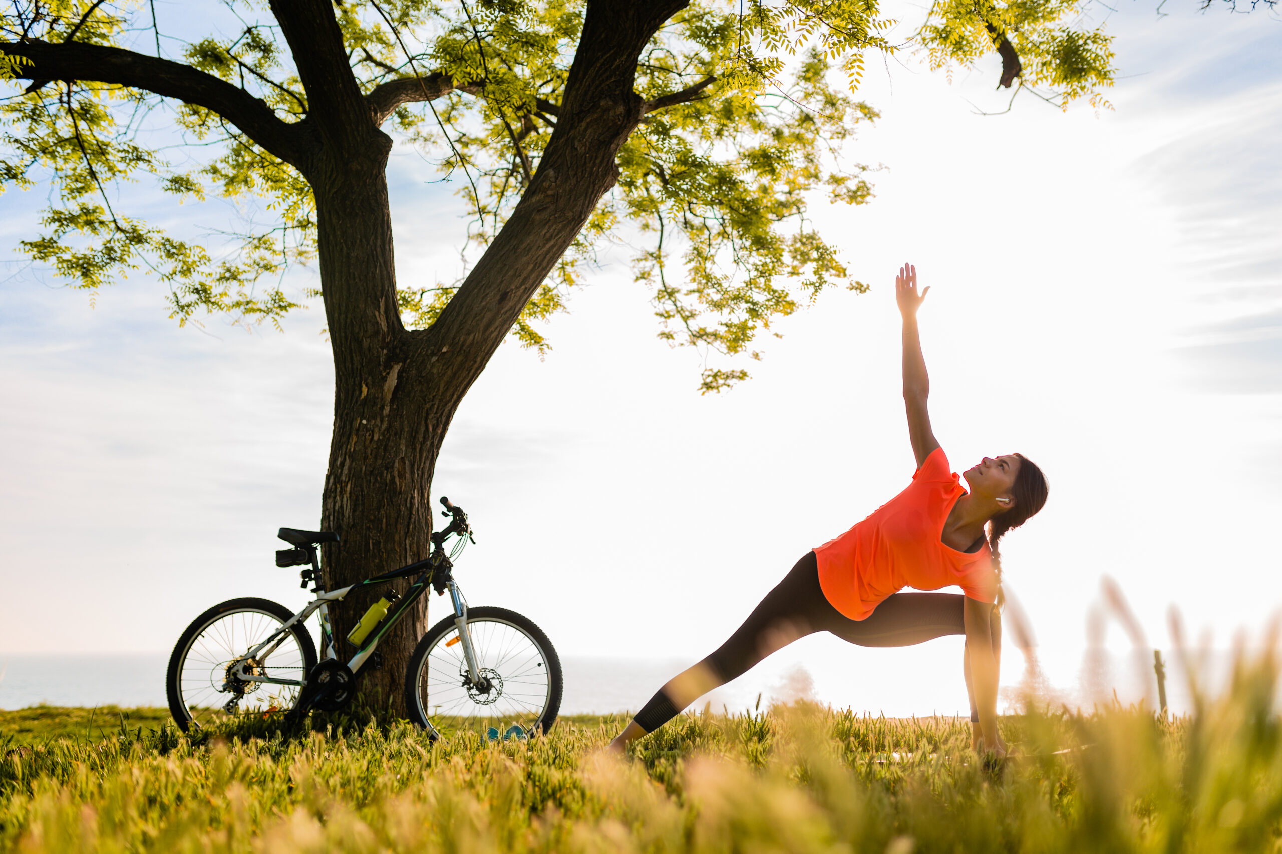 slim beautiful woman silhouette doing sports in morning in park doing yoga on mat in colorful fitness outfit in nature, smiling happy healthy lifestyle, calm meditation, bicycle on background